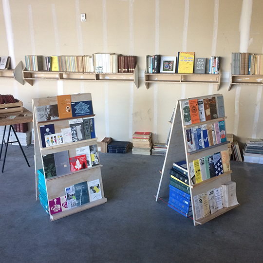 Several bookshelves display books inside a raw-walled library space.