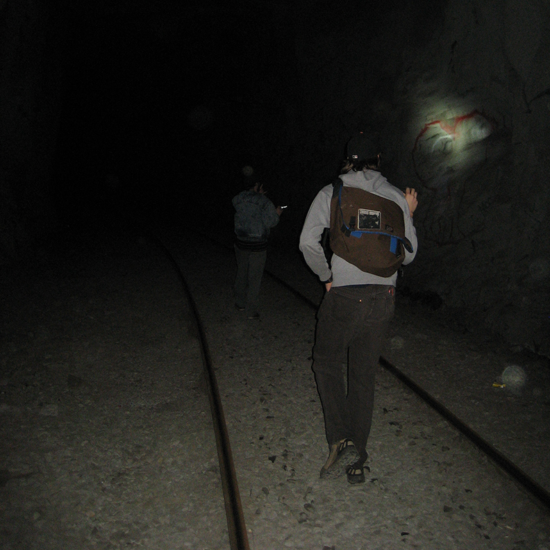 A person walking down a tunnel shines a light on the wall.